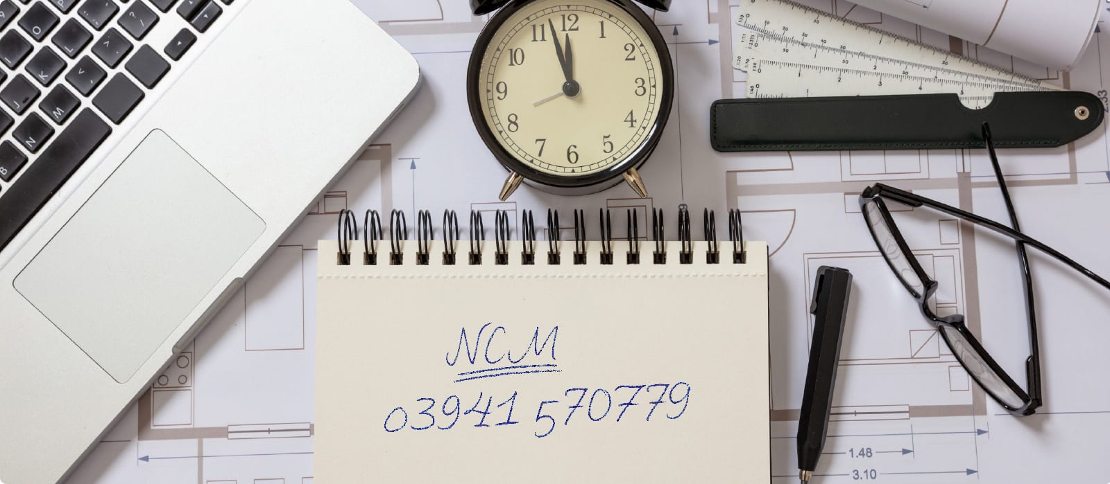 Notizbuch neben Uhr und Laptop auf einem Schreibtisch.