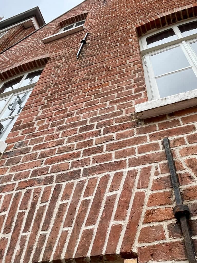 Backsteinfassade mit Fenstern und schwarzem Maueranker